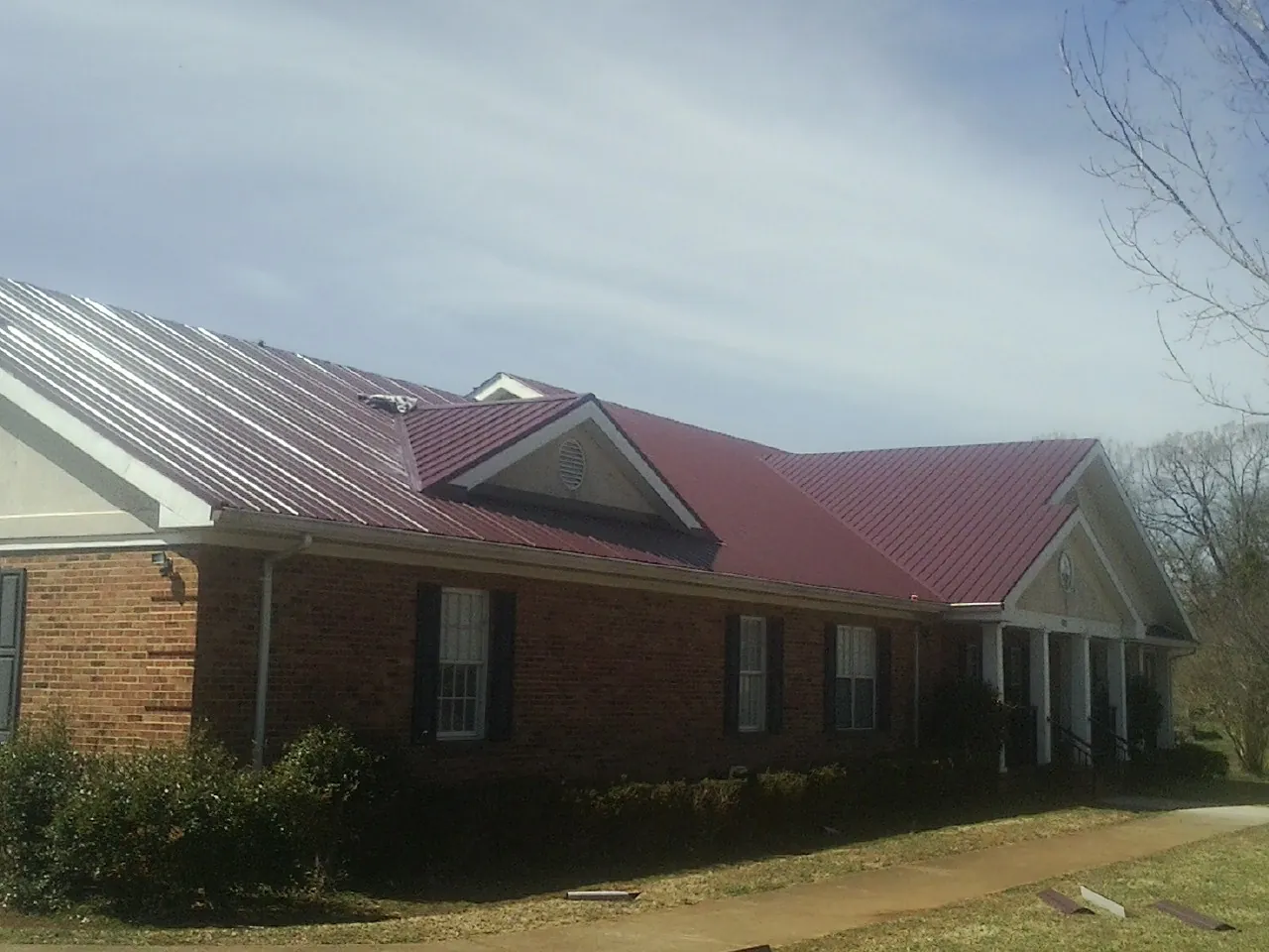 Red metal roof with gabled entries on a long brick building, from a Hail Damage Roof Repair job in Cottonport