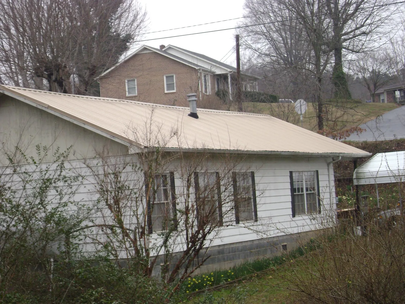Tan metal roof on a white sided house set into a hillside — Commercial Roofing by Roofing Brothers in Cottonport